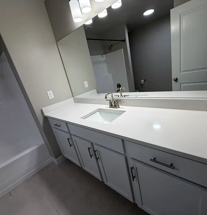 A clean bathroom vanity with a white counter and mirror